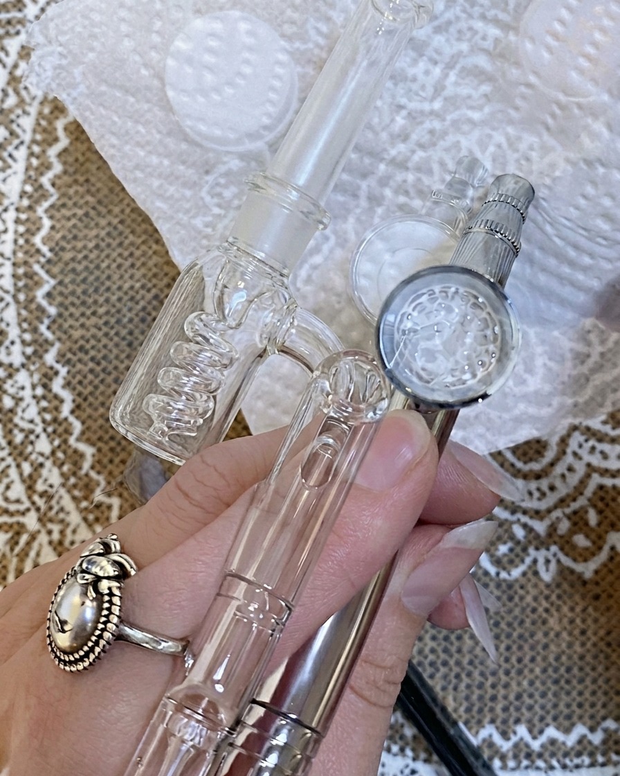 Airbrush-Anwendung mit feinem Farbnebel auf einer Nagelspitze über einer weißen Unterlage.