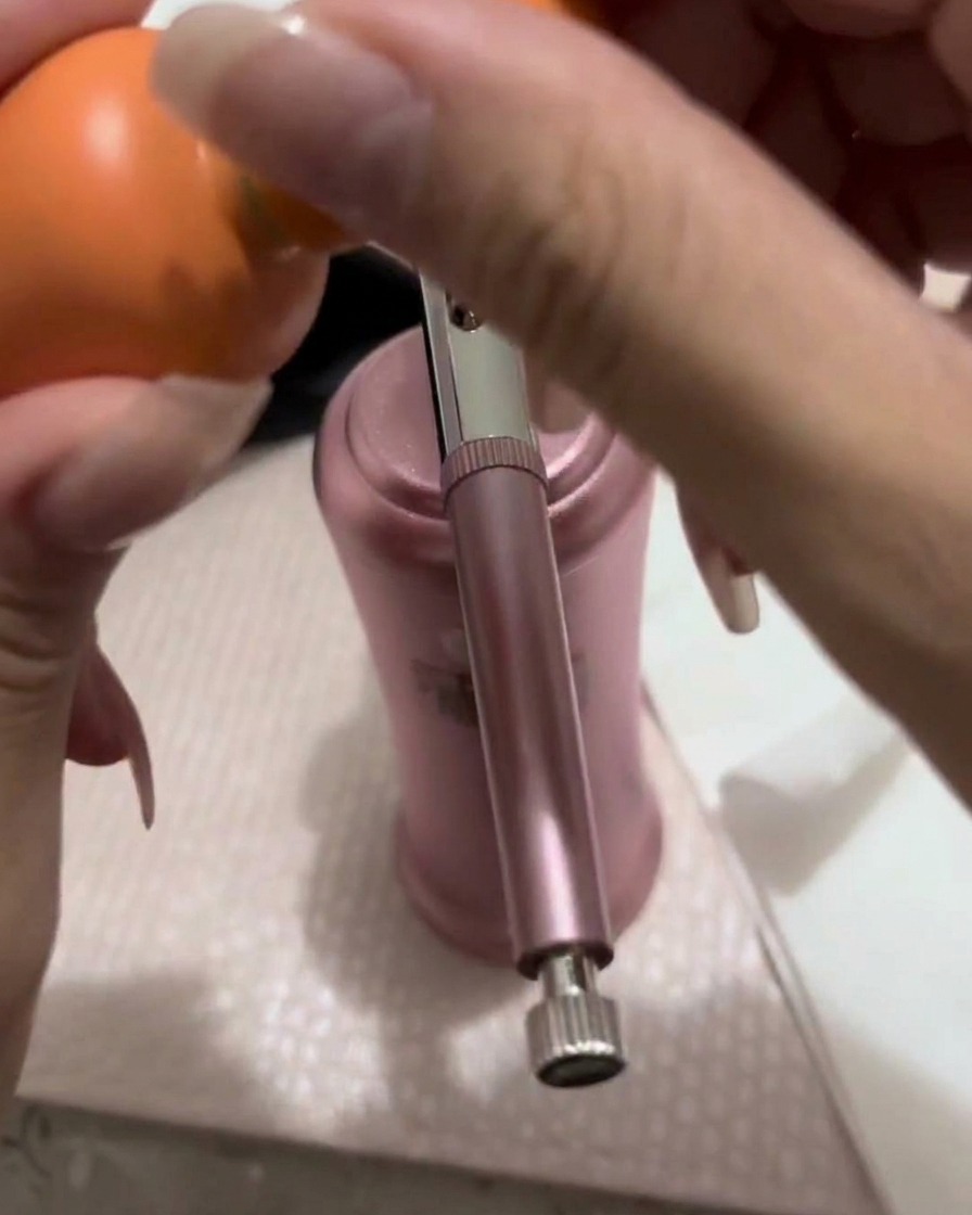 Eine kleine Menge pfirsichfarbenes Gel wird mit einem Pinsel in den Farbbecher einer Airbrush-Pistole gefüllt.