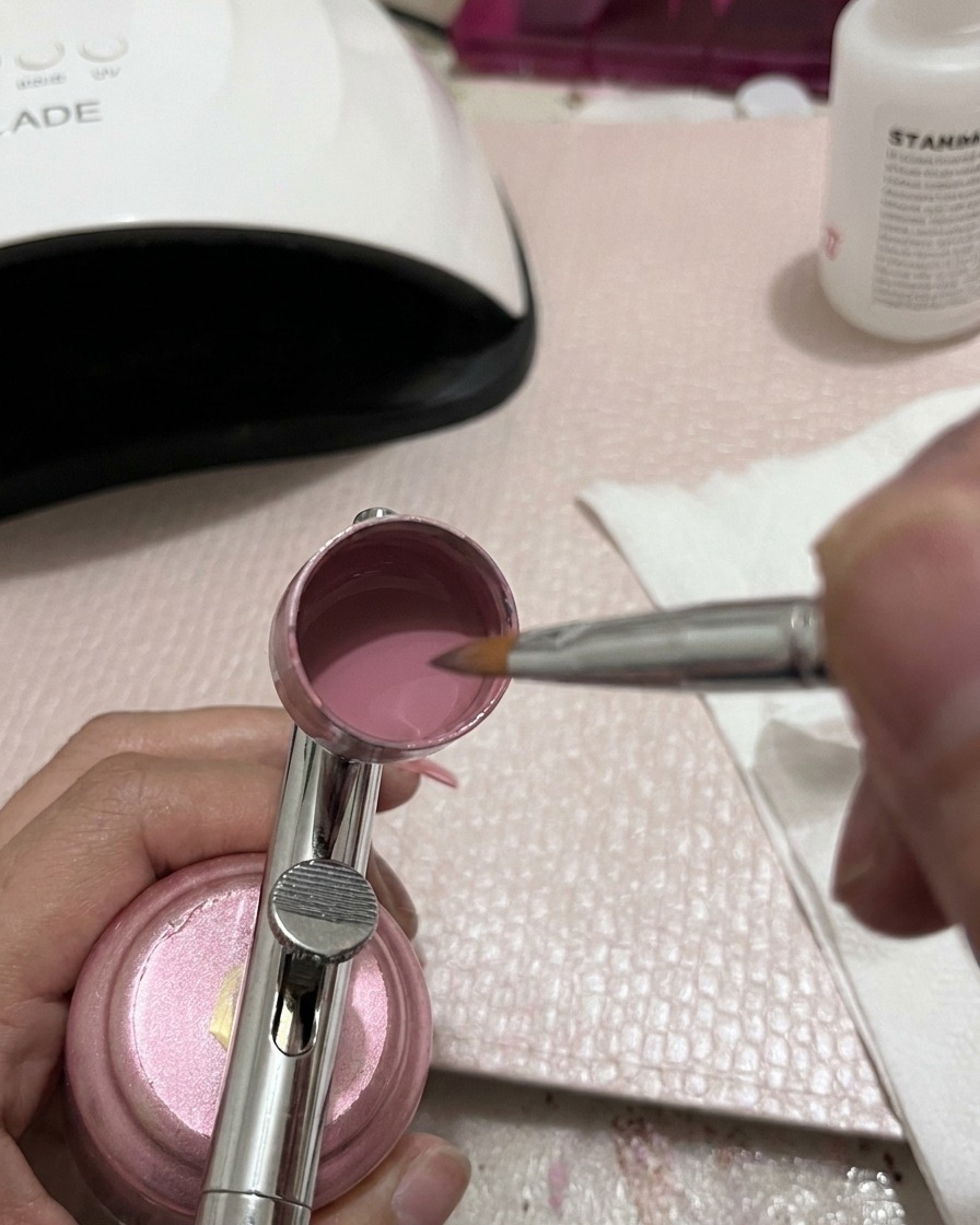 Nahaufnahme eines Werkzeugs zum Umrühren des rosa Gels im Airbrush-Becher.