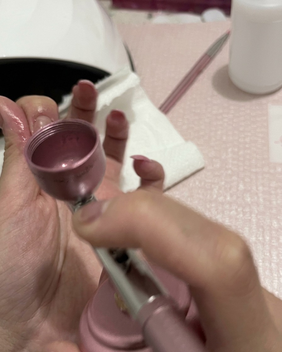 Nahaufnahme der Hände beim Airbrushen, wobei die Düse darauf ausgerichtet ist, die Farbe auf den Nägeln zu verblenden.
