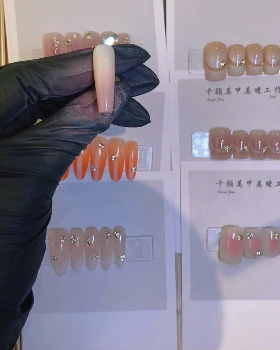 Nahaufnahme einer Pinzette, die einen kleinen glänzenden Kristall auf den Ansatz eines airgebrushten Nagels platziert.