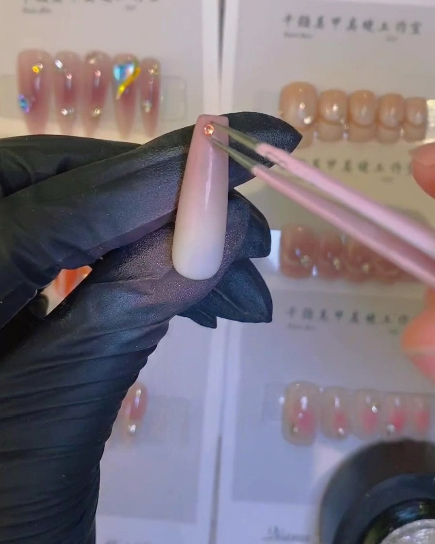 Ein Pinsel trägt einen klaren, glänzenden Überlack auf einen airgebrushten Ombré-Nagel mit Kristallverzierung auf.