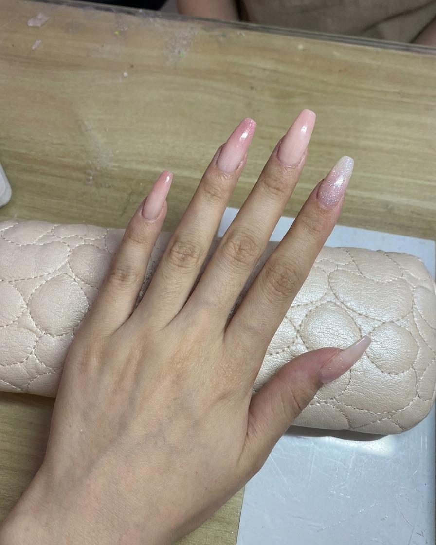 Eine Hand mit langen, hellen Nägeln wird mit einem zarten pinken Verlauf airgebrusht.