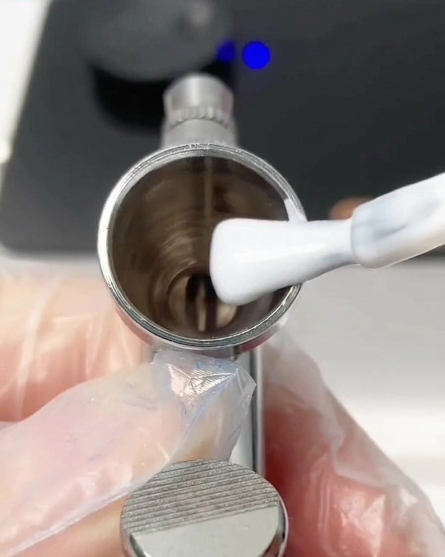 Ein Pinsel gibt einen Klecks weißes Farbgel in den Airbrush-Becher.