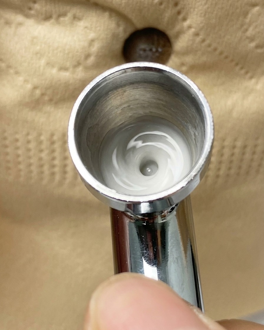 Eine Airbrush sprüht einen feinen weißen Farbnebel auf eine mit Klebeband halb abgedeckte Nagelspitze.