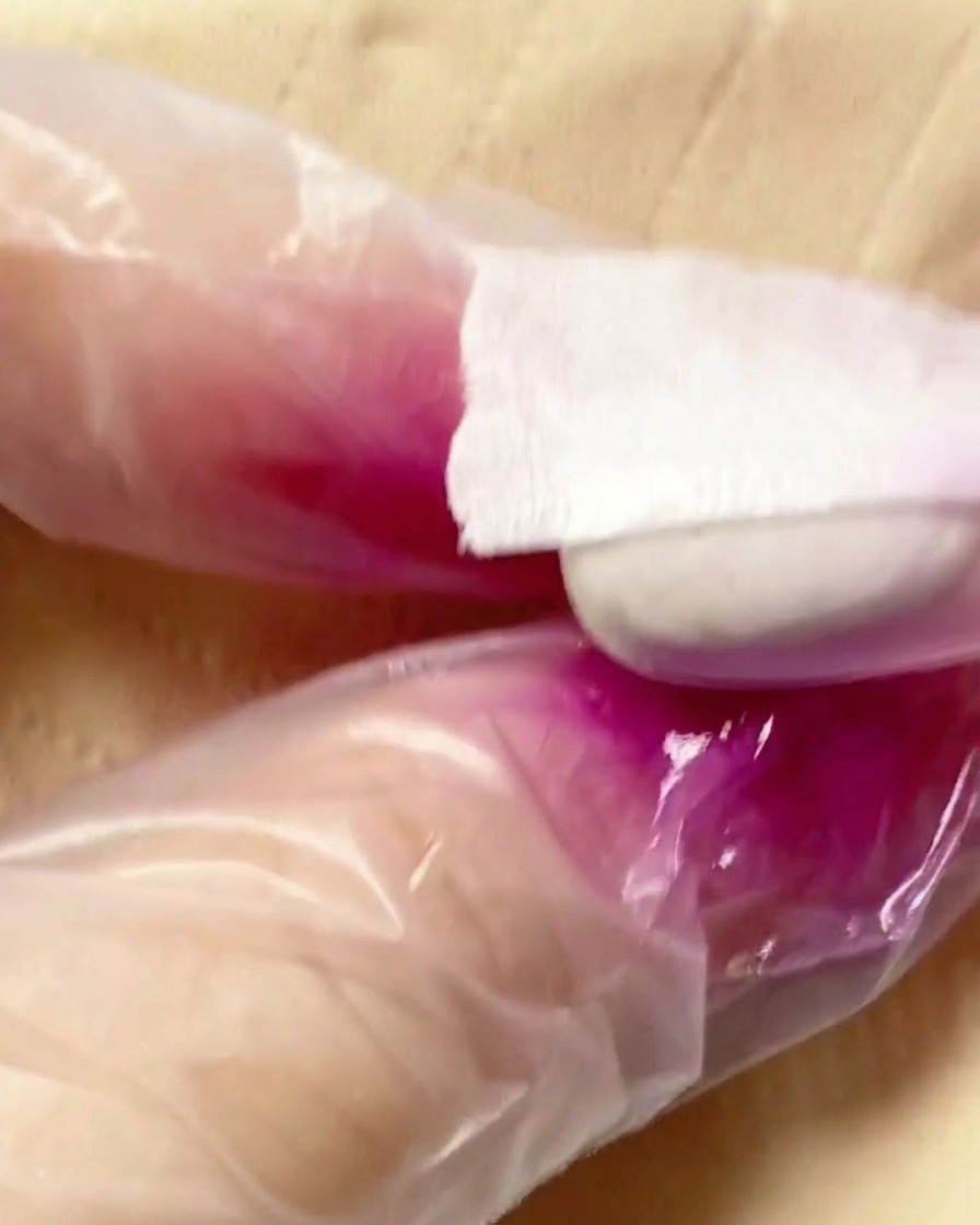 Eine Airbrush-Pistole sprüht lila Pigmentnebel auf die zweite Hälfte eines Nagel-Tips.