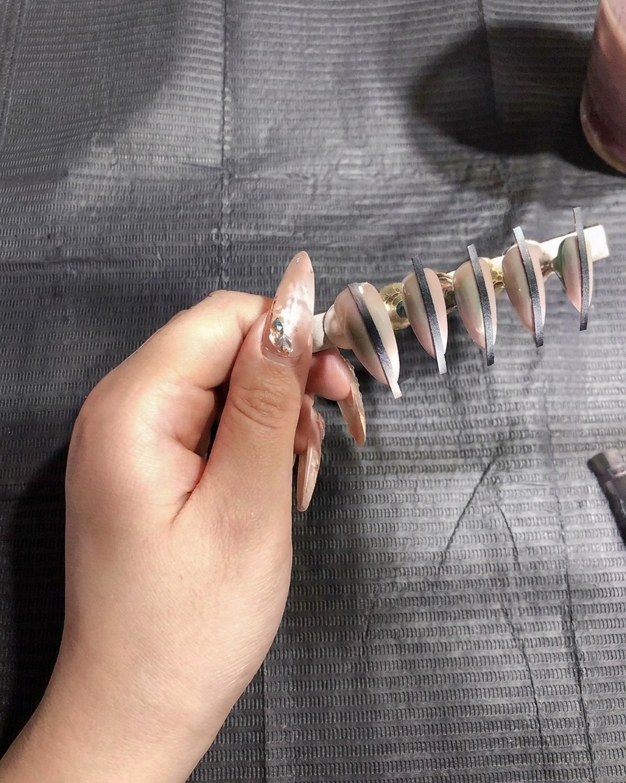 Eine Airbrush-Pistole sprüht eine dünne Schicht weißes Gel auf künstliche Nägel auf einem Ständer.