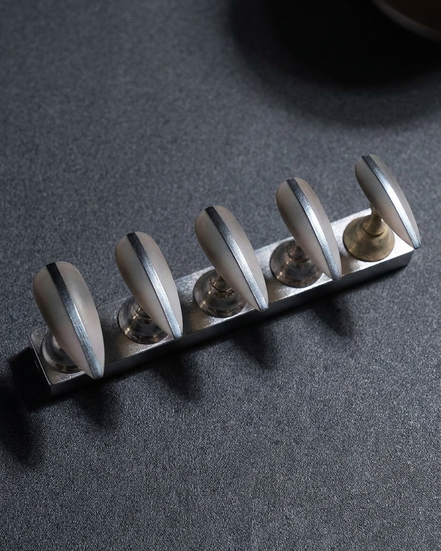 Nahaufnahme eines Metall-Nagelständers mit fünf Kunstnägeln; Fokus auf die Kantenbearbeitung mit einer Feile.