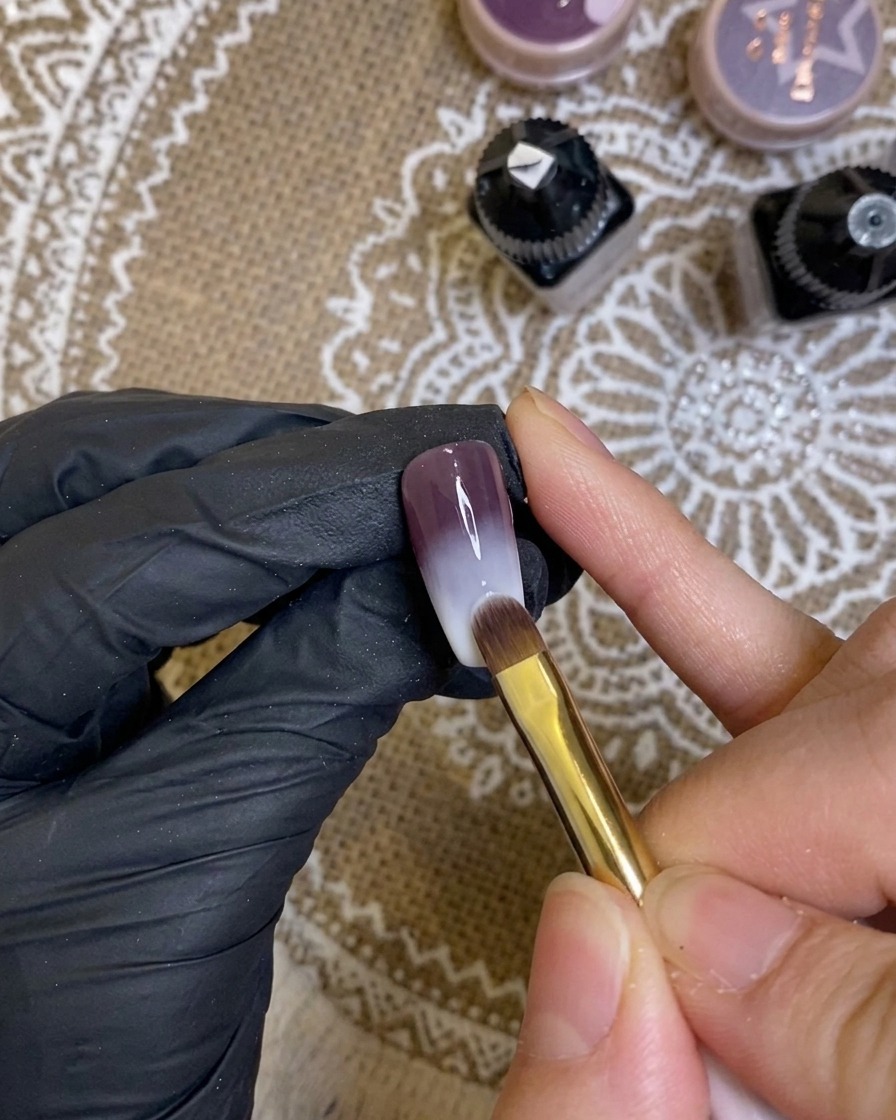 Detailansicht eines Pinsels, der sattes dunkles Lila-Gel auf eine Nagelspitze aufträgt.