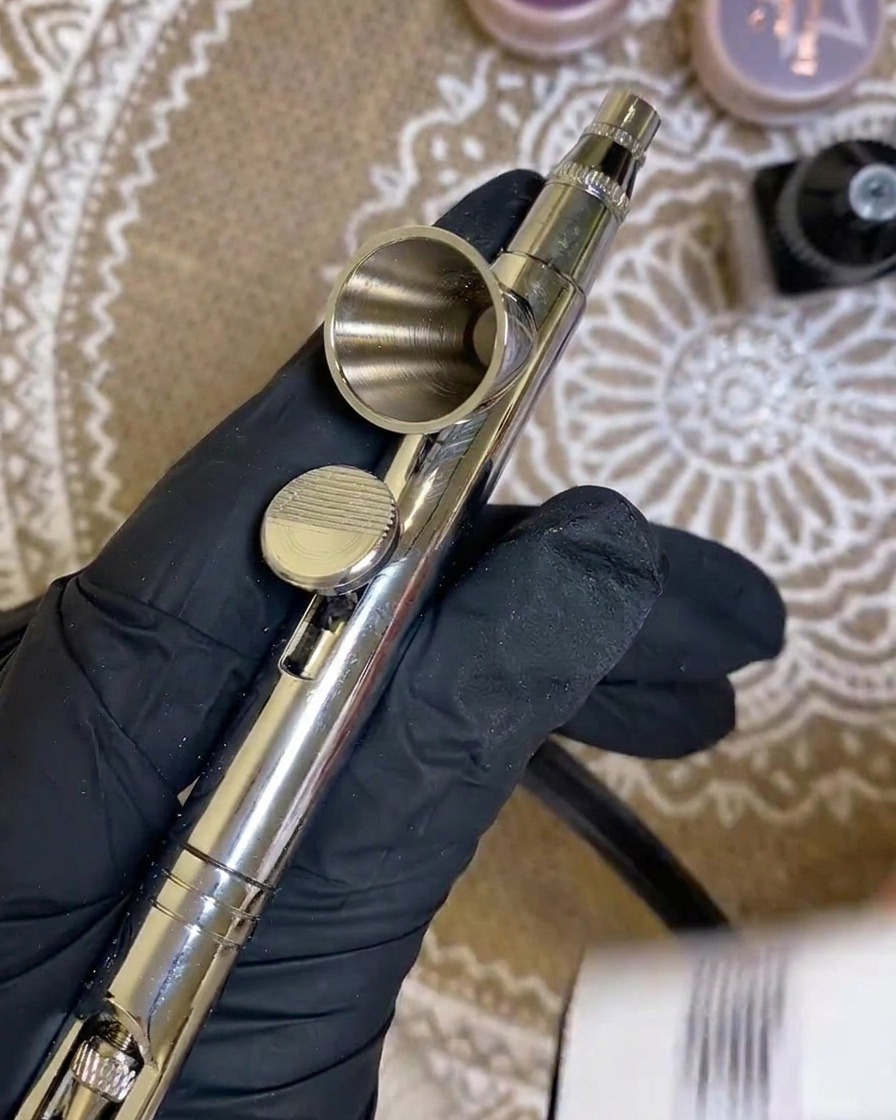 Nahaufnahme, wie weißes Gel in den kleinen Metallbehälter einer Airbrush-Pistole gefüllt wird.
