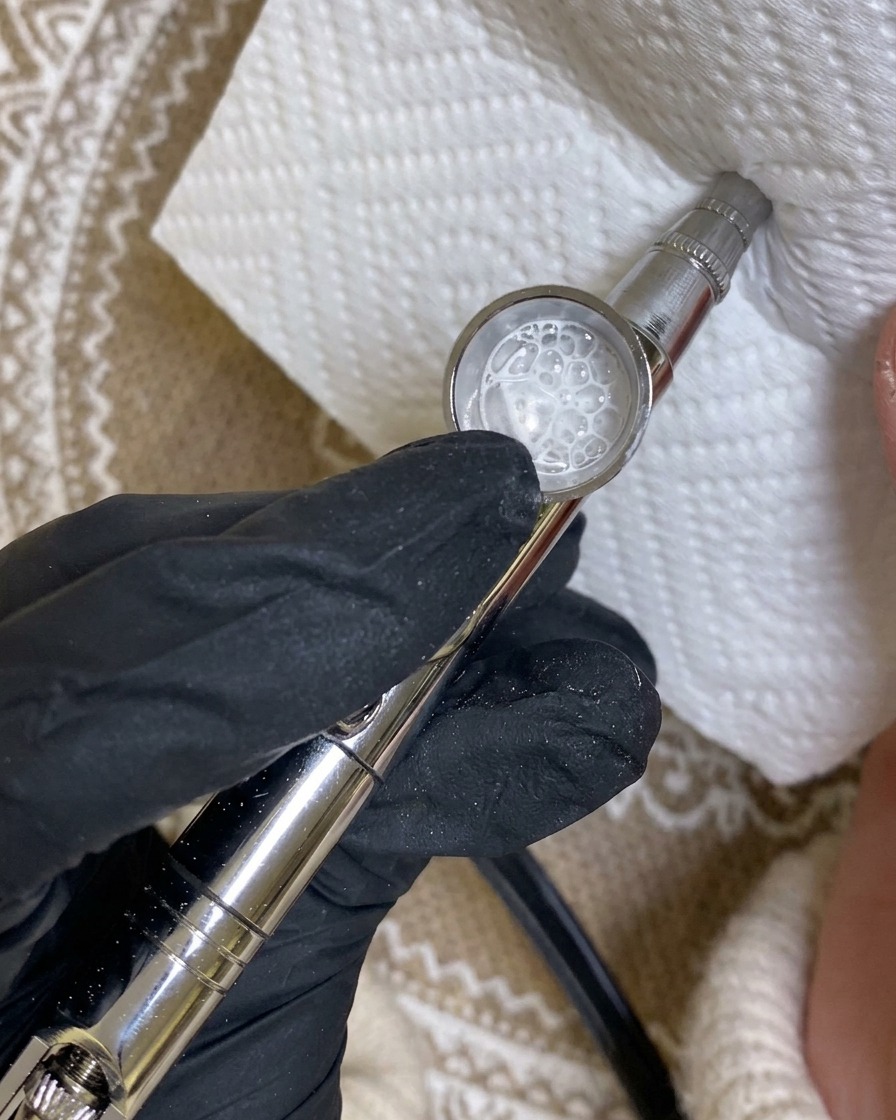 Eine Airbrush-Pistole sprüht auf ein Papiertuch, um das Sprühbild von weißer Farbe zu prüfen.