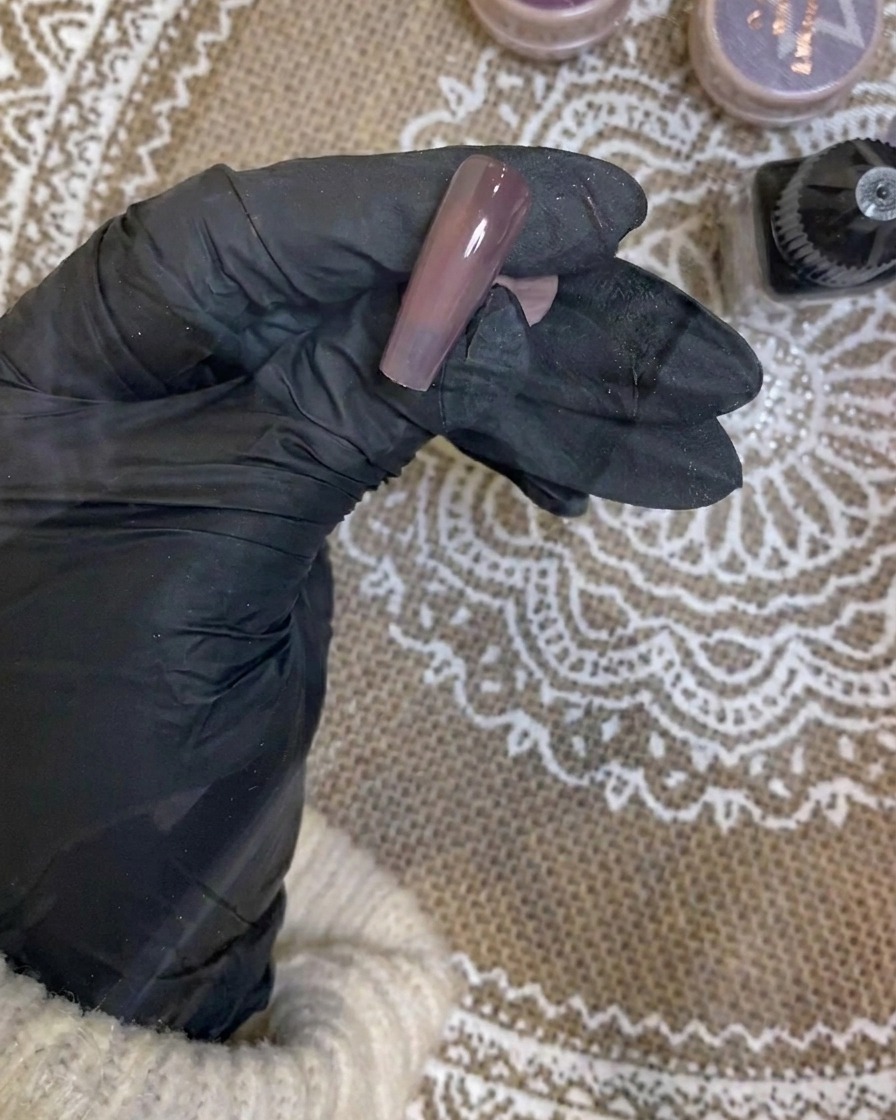 Ein Airbrush trägt einen sanften weißen Verlauf auf die Spitze eines dunkellila Nagels auf.