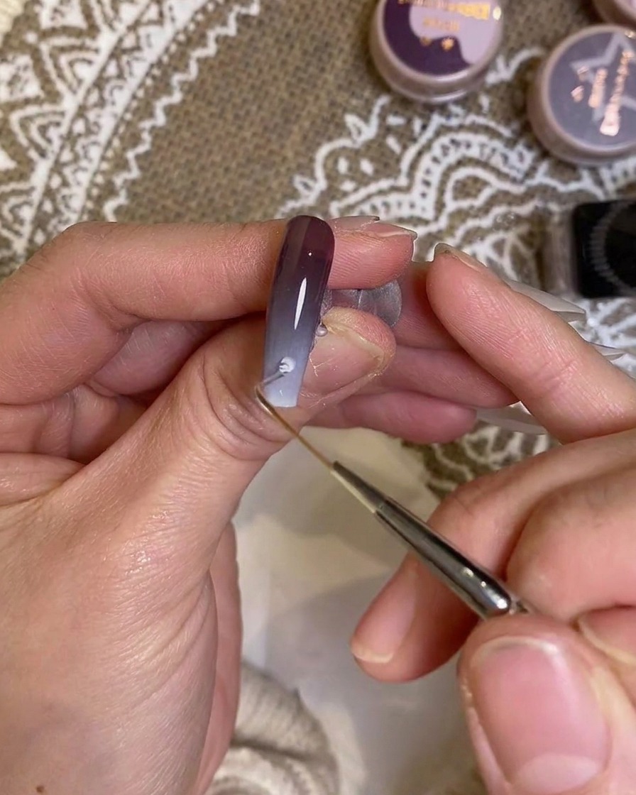 Ein Detailpinsel trägt präzise Farbe nahe der Nagelhaut auf.