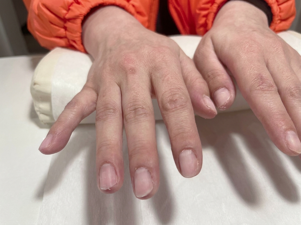 Nahaufnahme von zwei Händen mit vorbereiteten, klaren Gelnägeln auf einem weißen Salon-Kissen.