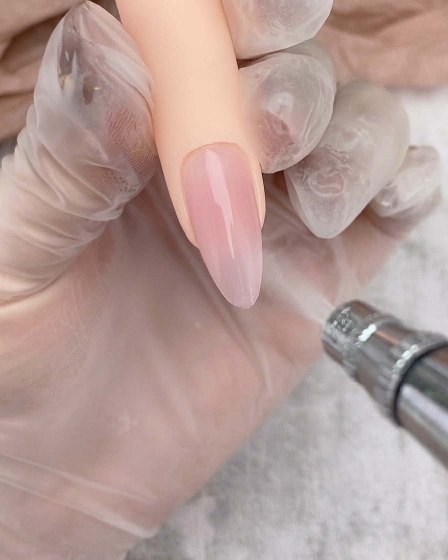 Ein Airbrush-Gerät trägt einen sanften weißen Verlauf auf die Spitze eines mit Gel beschichteten Nagels auf.