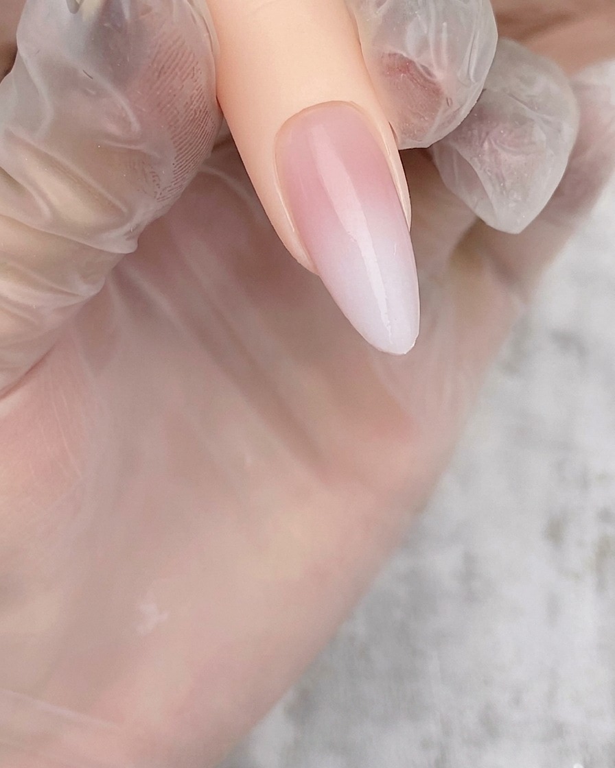 Ein mandelförmiger Nageltipp mit einem zarten, halbtransparenten weißen Airbrush-Verlauf über einer Nude-Basis.