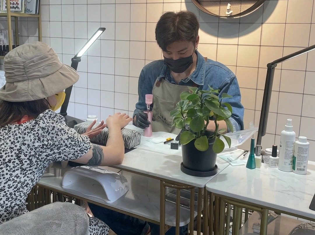 Eine Nageldesignerin trägt mit einem kleinen Pinsel vorsichtig klaren Base-Gel auf den Fingernagel eines Kunden auf.