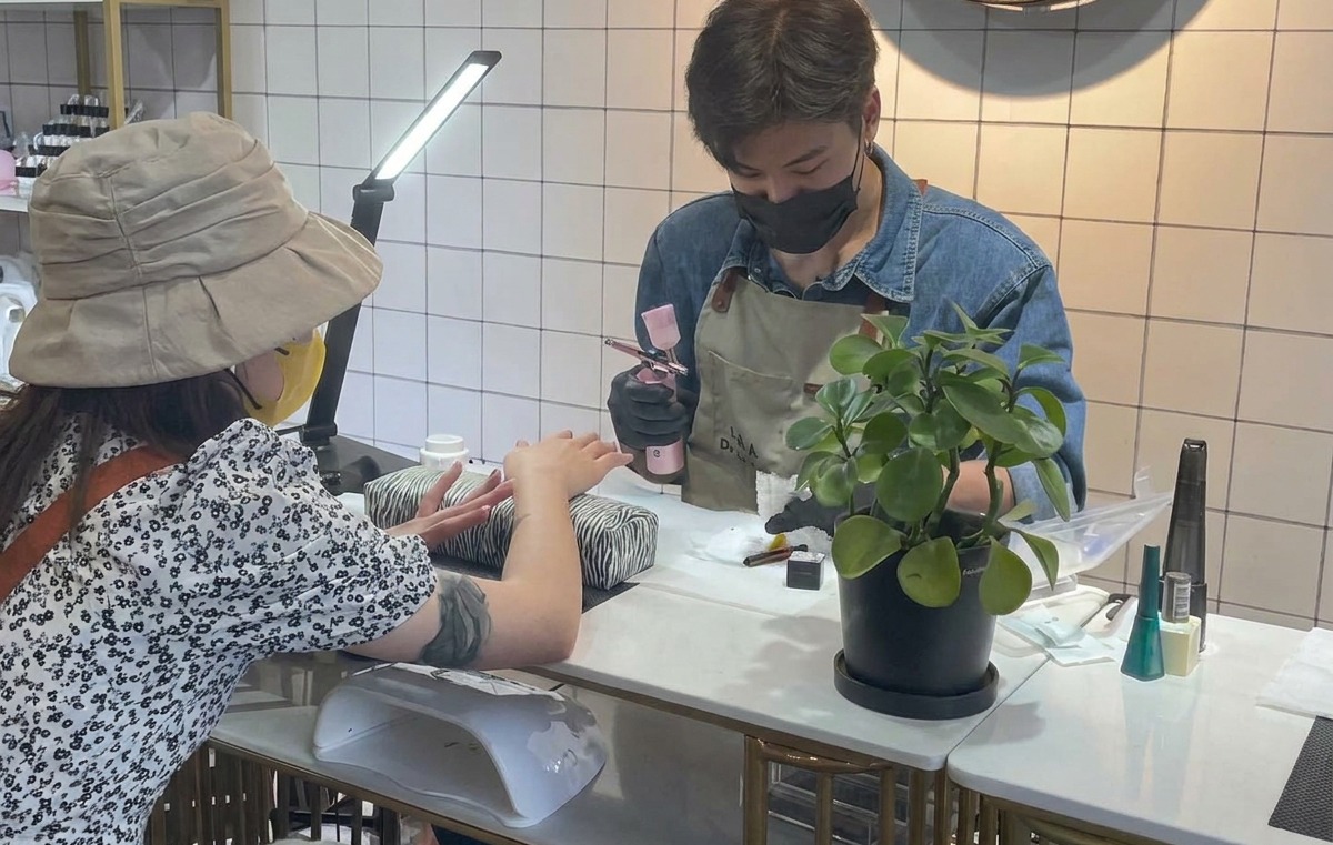 Eine Nageldesignerin hält eine Airbrush-Pistole und testet das Sprühbild auf einem weißen Papiertuch.