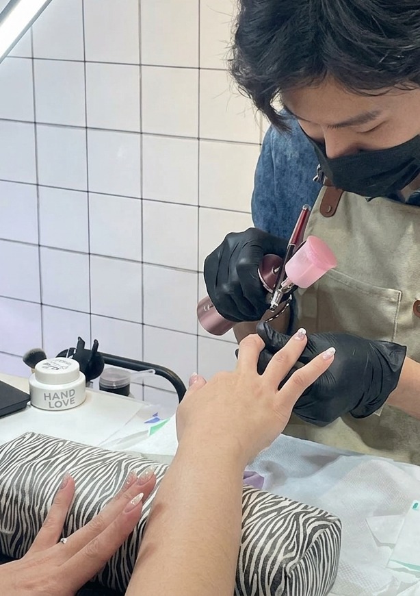 Eine extreme Nahaufnahme, wie ein feiner violetter Nebel aus einer Airbrush-Pistole auf die Nagelspitze gesprüht wird.