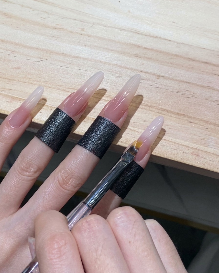 Ein Ombré-Pinsel, der mit leichten, wischenden Bewegungen den Rand des weißen Gels auf einem Stiletto-Nagel verwischt.