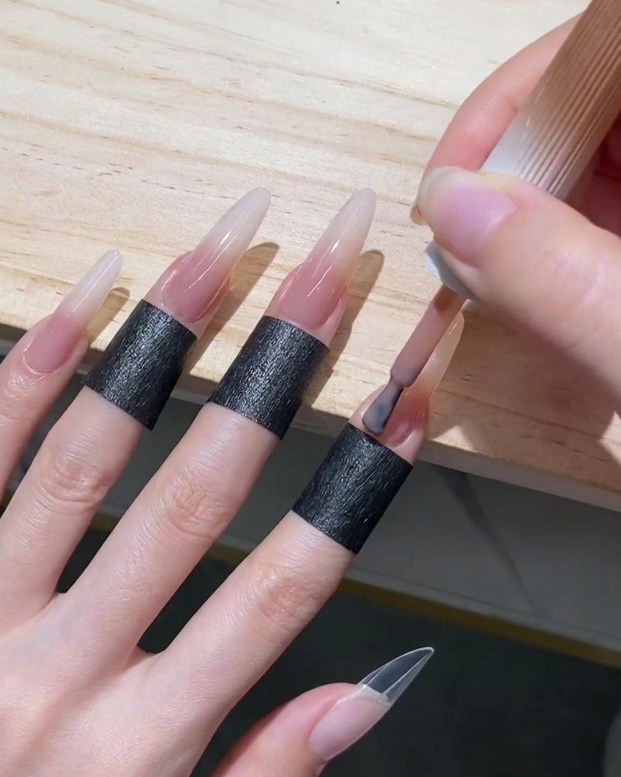 Auftragen eines zarten, nude-rosafarbenen Gel-Lacks auf den Nagelhautbereich und die untere Hälfte eines langen Stiletto-Nagels.