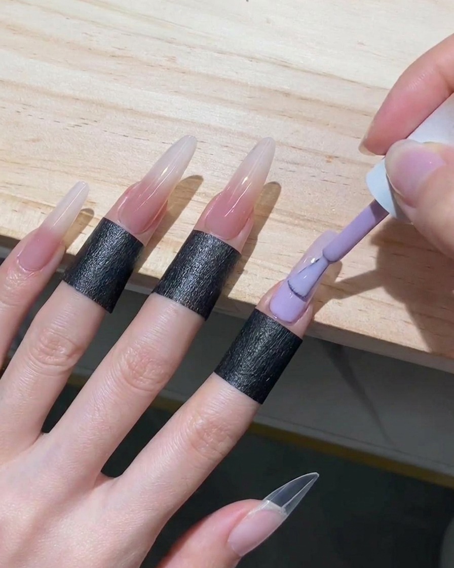 Ein Gel-Pinsel füllt die untere Hälfte eines Stiletto-Nagels mit zartem Nude-Gel auf und führt es bis an den verwischten weißen Rand heran.