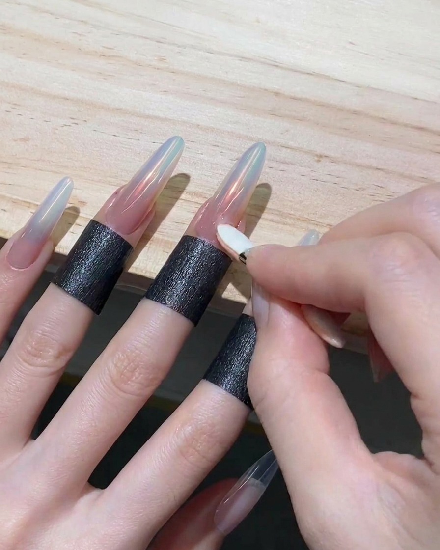 Eine Hand reibt mit einem kleinen Lidschatten-Applikator irisierendes orangefarbenes Puder auf die Spitze eines langen Nagels.