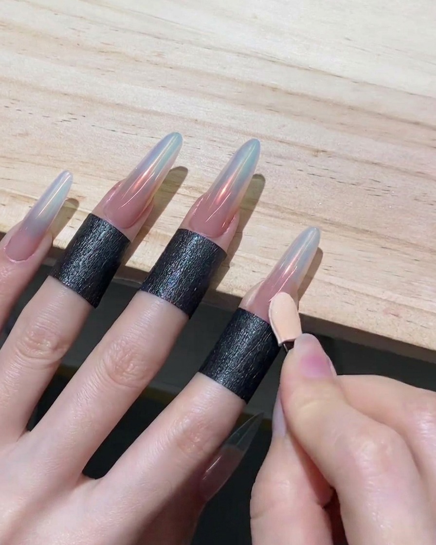 Eine Hand zieht mit der sauberen Seite eines Lidschatten-Applikators Chrompuder auf einem Nagel nach unten und erzeugt so einen Ombré-Effekt.