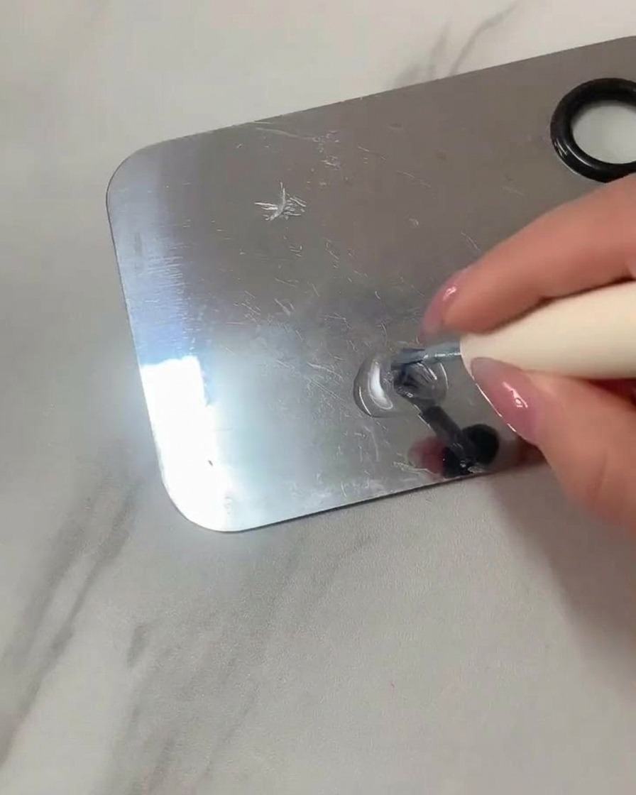 Ein flacher Gelpinsel mischt klares Gel und hellblauen Lack auf einer Make-up-Palette aus Edelstahl.