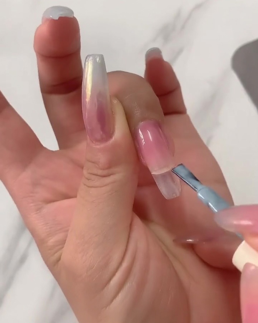 Nahaufnahme eines Gelpinsels, der hellblauen UV-Lack auf die obere Hälfte eines langen, klaren Coffin-Nageltips aufträgt.