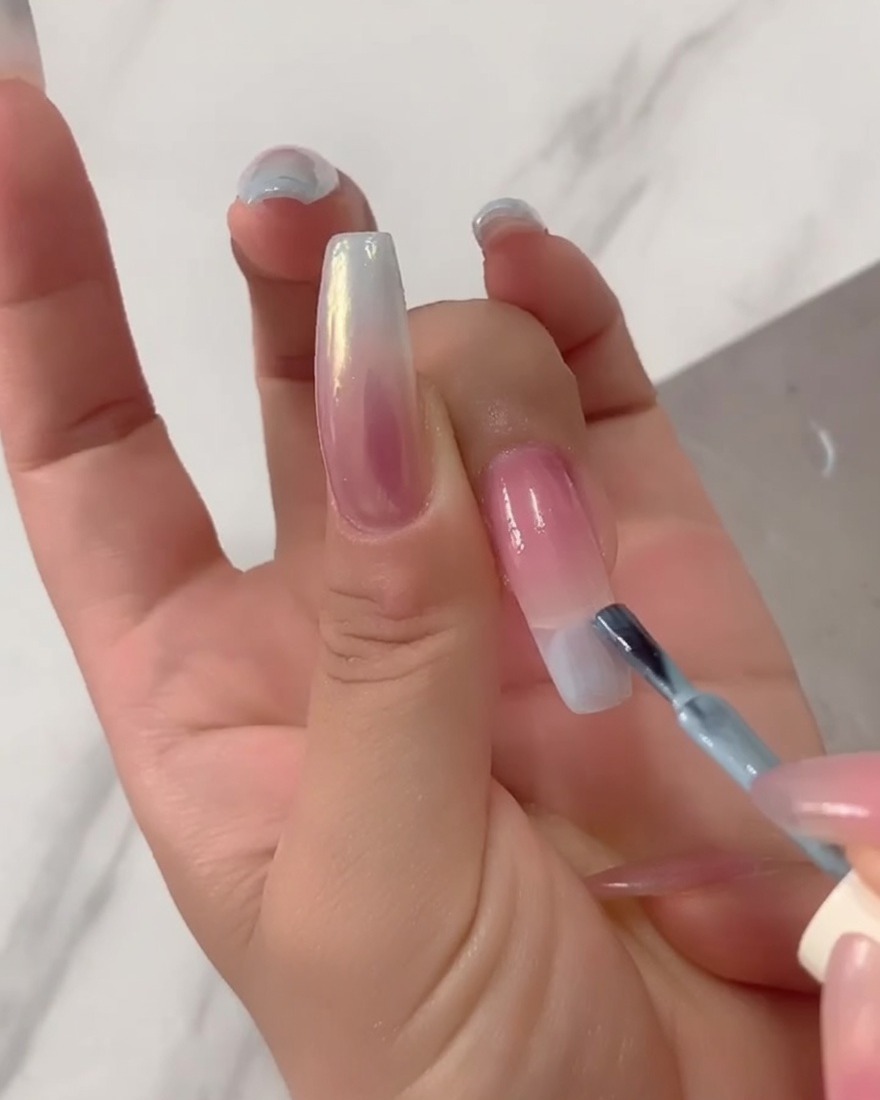 Nahaufnahme eines Pinsels, der deckenden hellblauen UV-Lack direkt auf die Spitze einer langen Nagelverlängerung aufträgt.