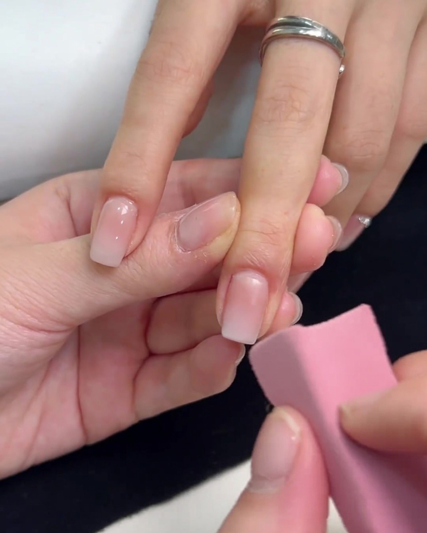 Ein rosa Schwamm tupft weißen Gel-Lack auf die Spitze eines quadratischen Nagels.