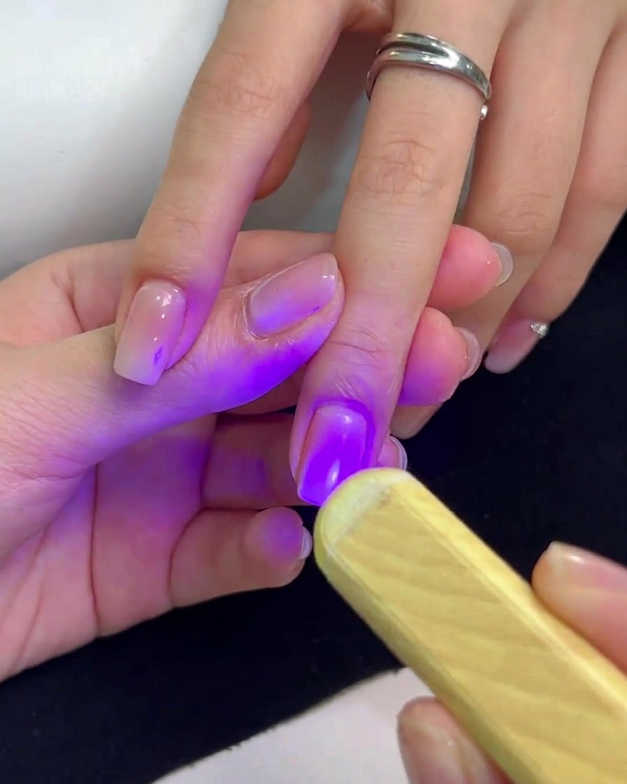 Eine kleine Hand-UV-Lampe mit violettem Licht über dem Fingernagel.