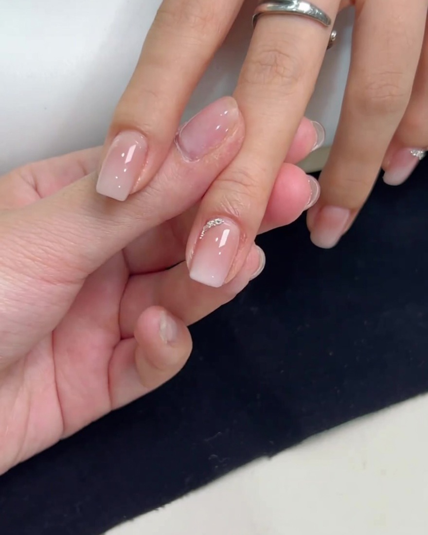 Ein quadratischer Nagel mit einer Reihe aus kleinen silbernen Steinen und Kügelchen entlang der Nagelhaut.