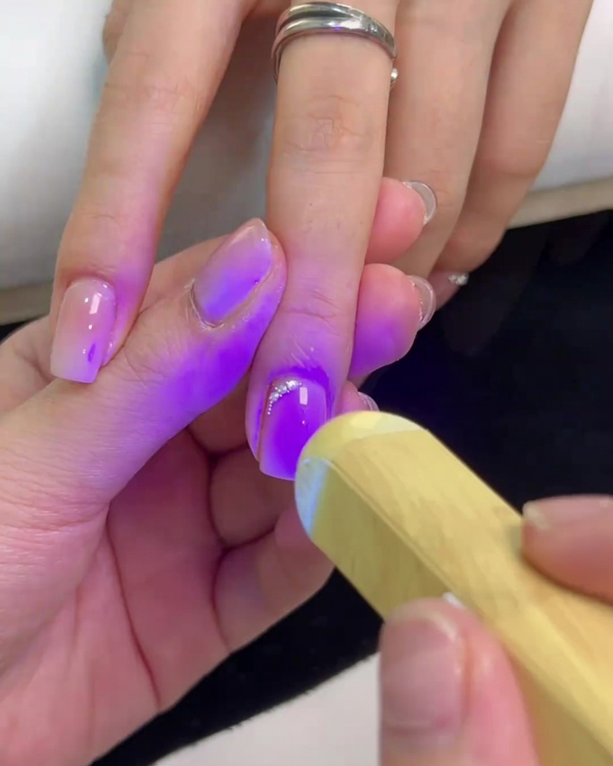 Eine kleine Hand-UV-Lampe beleuchtet den Nagel, um den Kleber und die Steine auszuhärten.