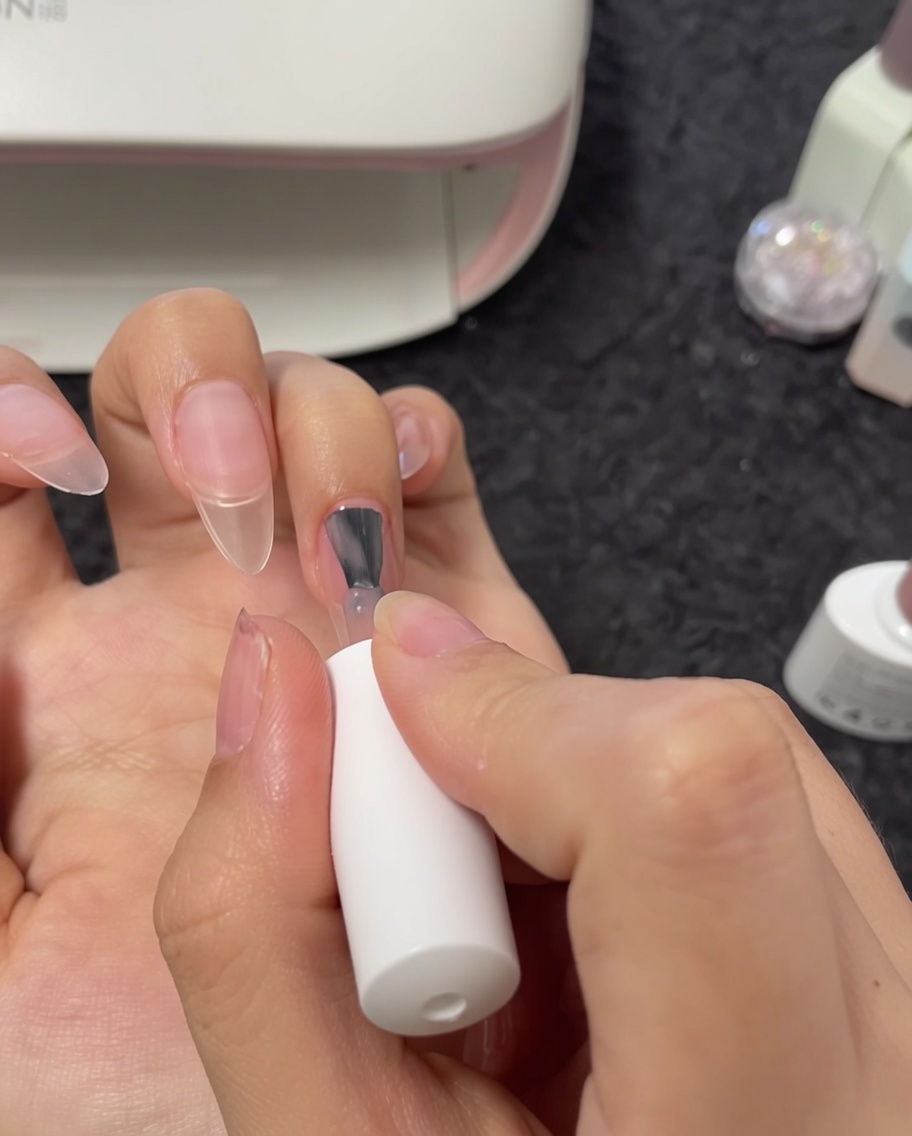 Eine Nahaufnahme von einem Pinsel, der Nude-Gel auf den Mittelfingernagel aufträgt.