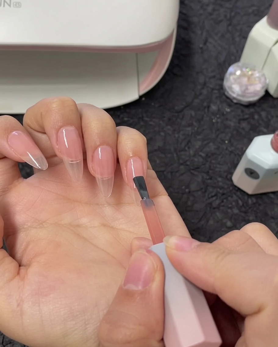 Ein Pinsel trägt eine zweite Schicht Nude-Gel auf den Zeigefingernagel auf.
