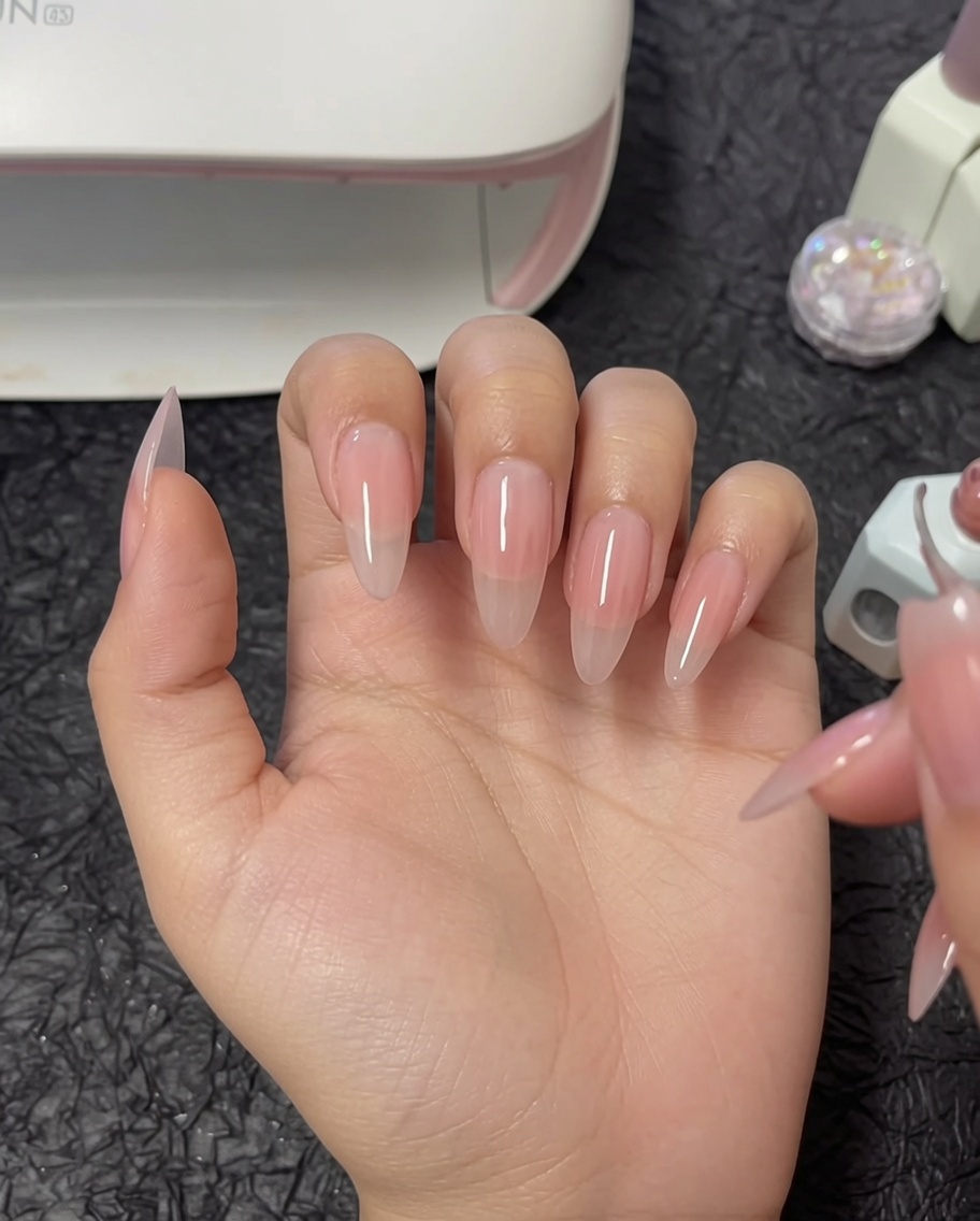 Ein Pinsel trägt eine zweite Schicht Nude-Gel auf den Daumen auf.
