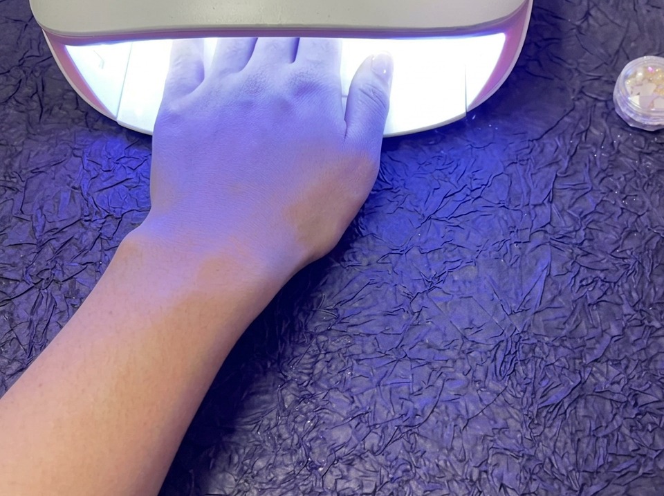 Eine Hand liegt zum Aushärten in einer leuchtenden UV/LED-Lampe auf einer lila Oberfläche.