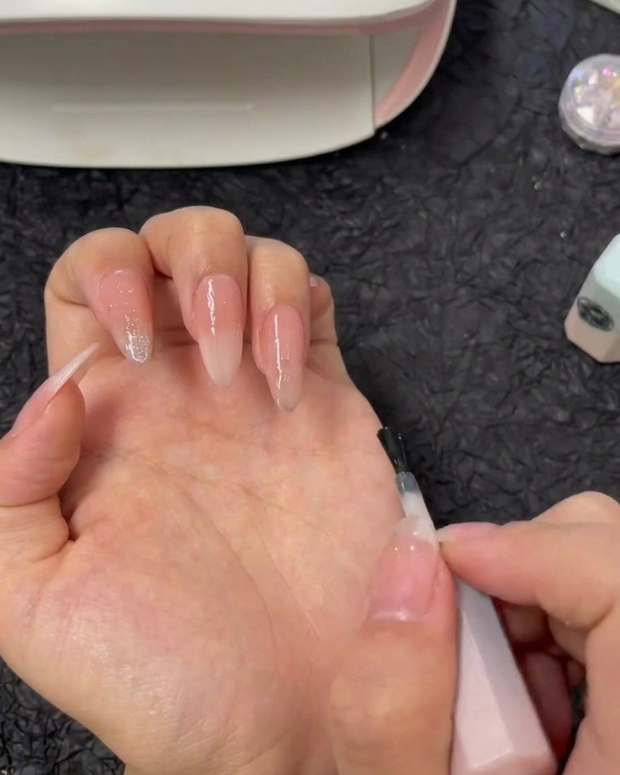 Ein Pinsel trägt klares Verstärkungsgel direkt auf einen Zeigefinger mit Ombré-Verlauf auf.