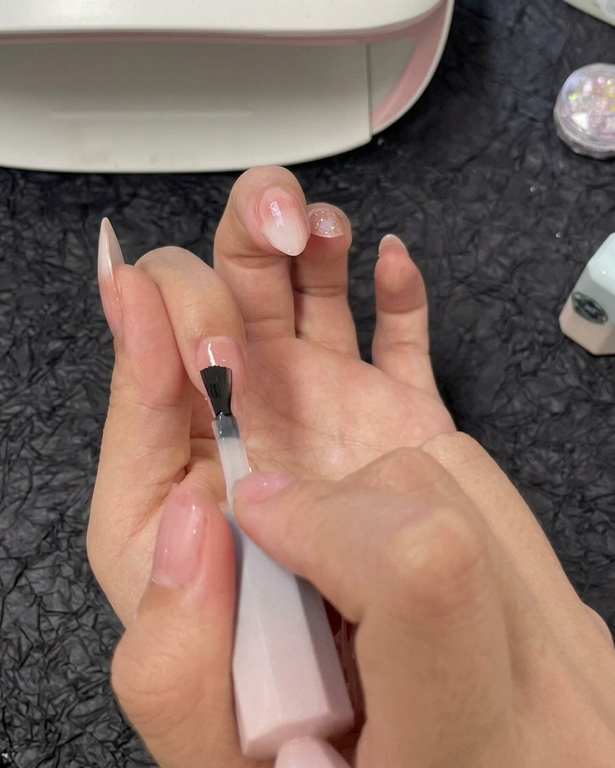 Ein Pinsel trägt eine Schicht klares Aufbaugel über dem Ringfingernagel auf.