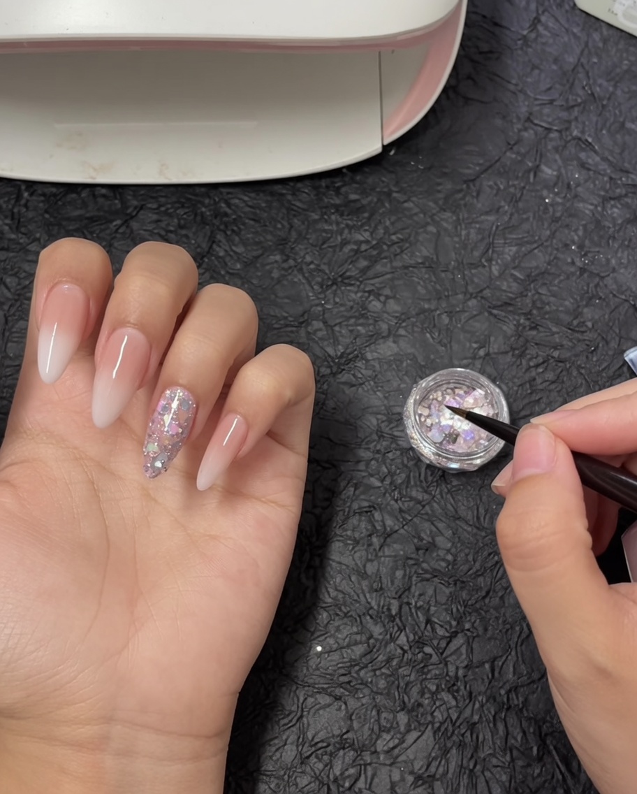 Ein feiner Nailart-Pinsel tunkt in ein kleines Töpfchen mit schillernden, groben Glitter-Flakes.