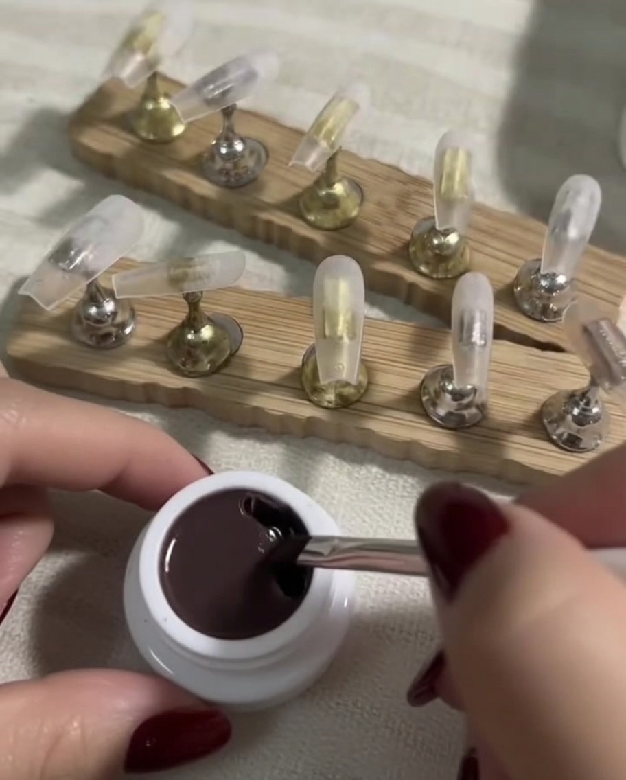 Ein flacher Gel-Pinsel taucht in einen kleinen Tiegel mit dunklem Nude-Gel.