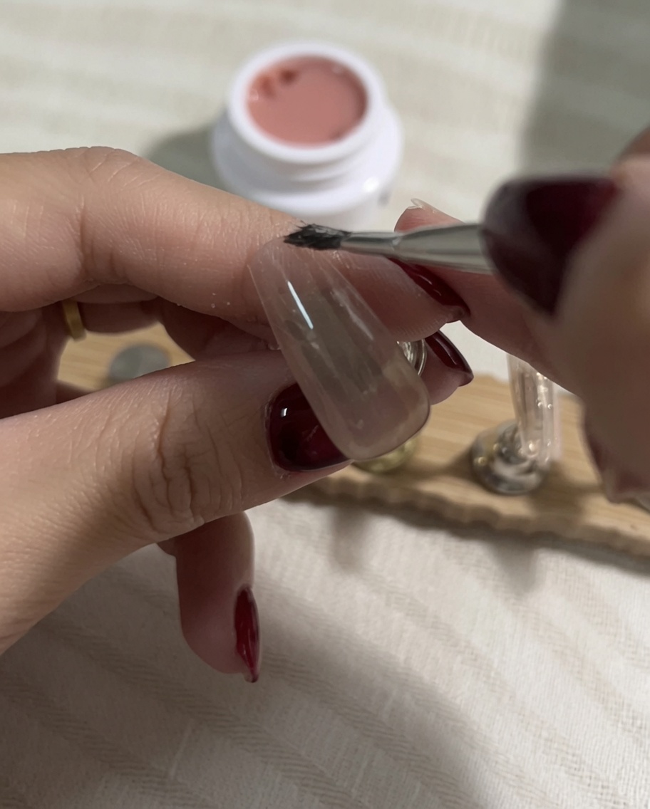 Aufnehmen eines helleren Nude-Gels mit einem flachen Pinsel nach dem Aushärten der vorherigen Schicht.