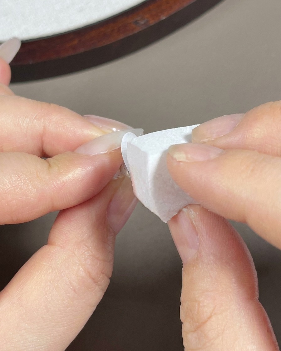 Ein Make-up-Schwamm tupft weißes Gel auf die Spitze eines langen Mandel-Nagels.