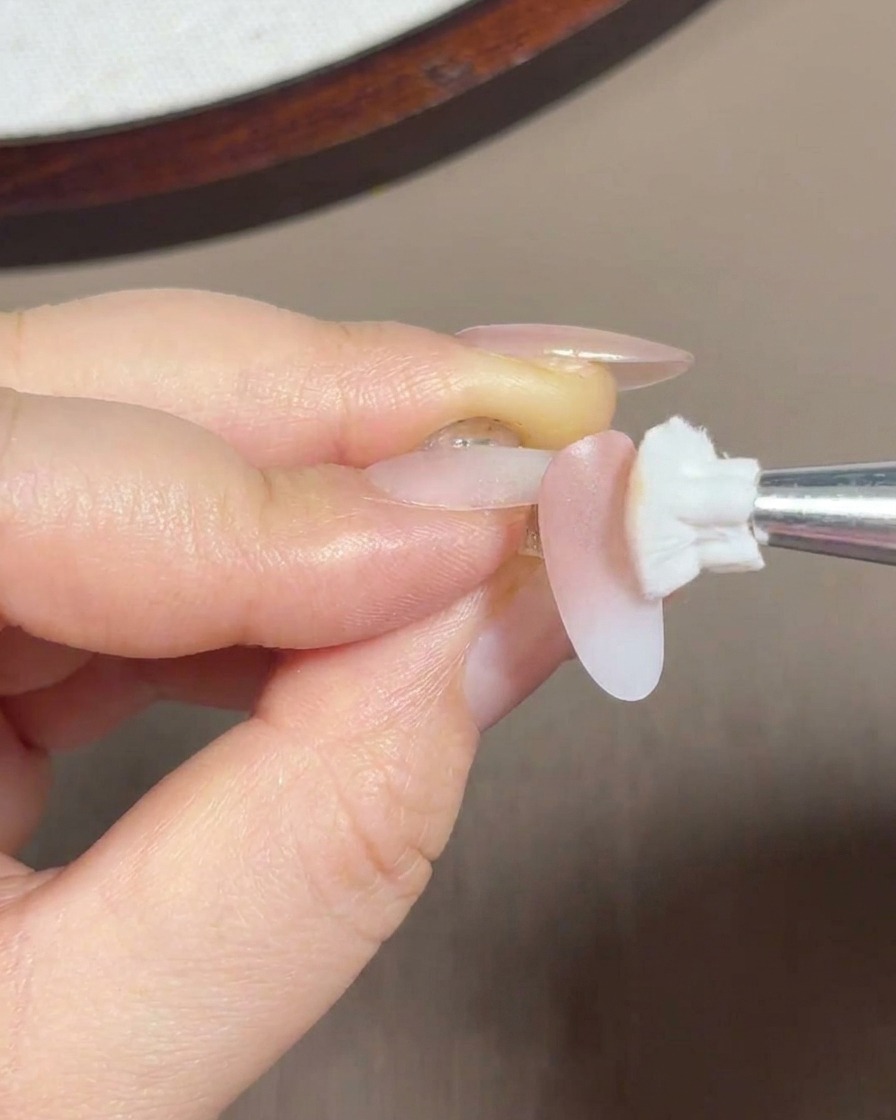 Ein Schwammpinsel verblendet rosa Gel auf der hinteren Hälfte und dem Nagelhautbereich des Nagels.