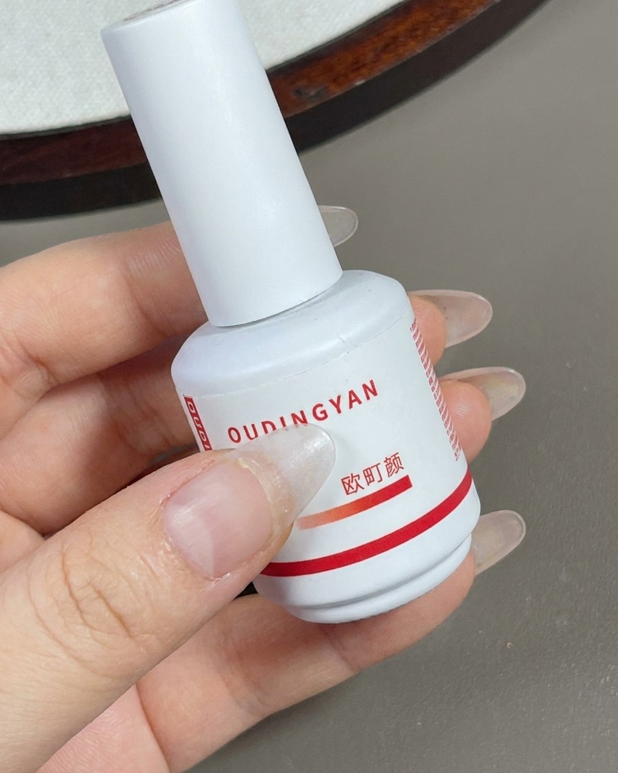 Ein Pinsel trägt eine Schicht transparentes Nude-Gel über die gesamte Nageloberfläche auf.