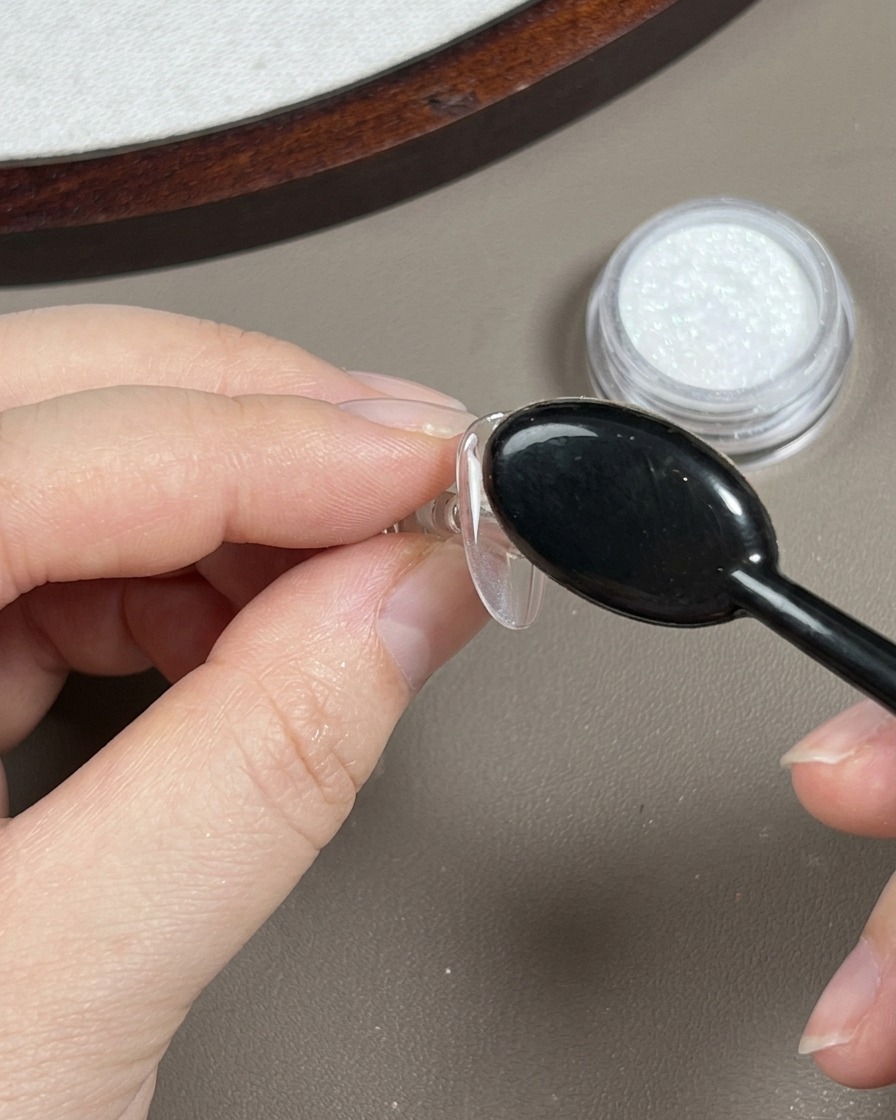 Ein schwarzer Staubpinsel wischt über einen Nagel, um loses, durchscheinendes Chrom-Puder zu entfernen.
