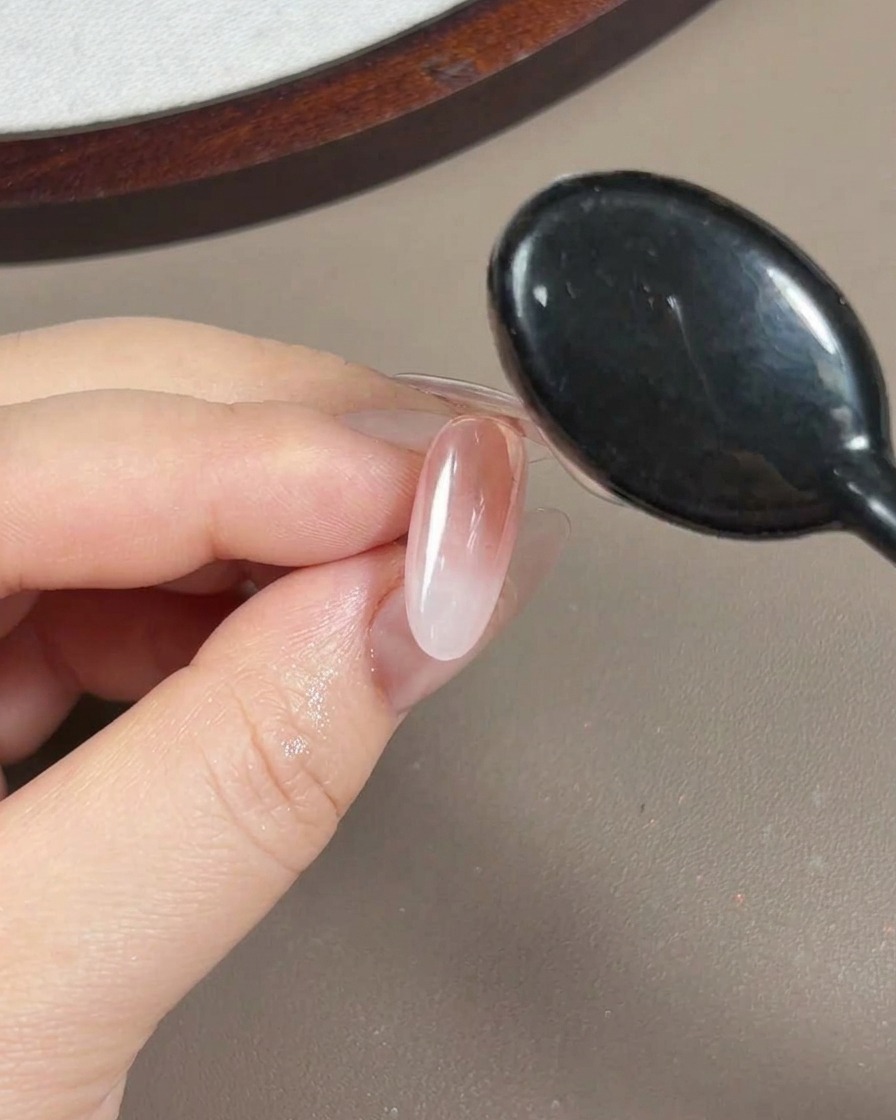 Nahaufnahme beim Auftragen eines klaren, viskosen Aufbau-Gels über einen Nagel mit Aurora-Puder.
