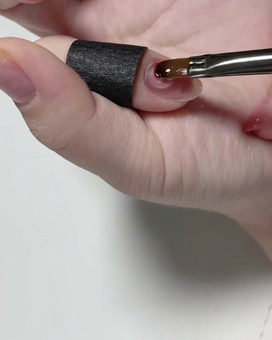 Ein Detailpinsel trägt klares Struktur-Gel auf einen Naturnagel auf.